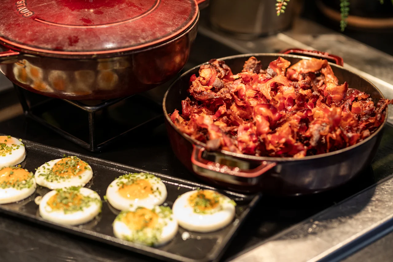 A delicious breakfast spread at Home Hotel Grand Bodø featuring crispy bacon, perfectly cooked eggs with chives, and a warm pot.