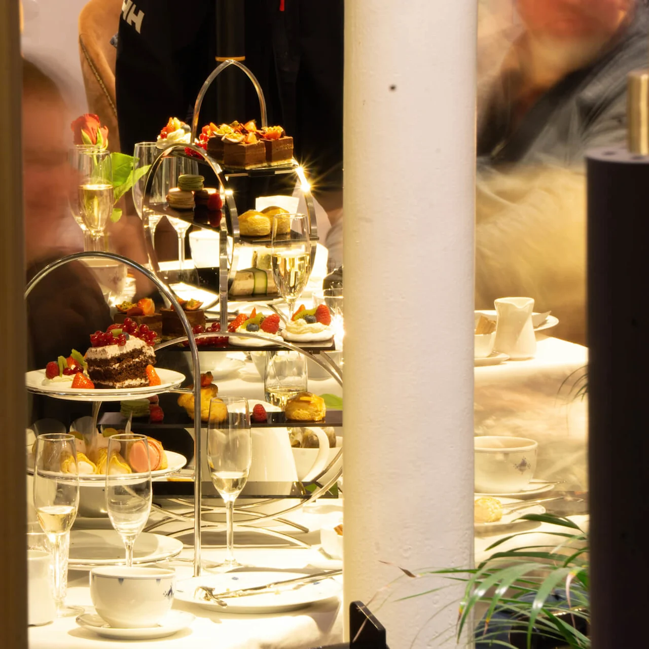 An elegant afternoon tea service displayed on tiered trays with cakes and pastries, inside a cozy café setting.