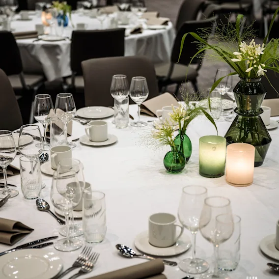 A formal dining table set for an event, with multiple place settings, green floral centerpieces, and glowing candles creating a warm ambiance.