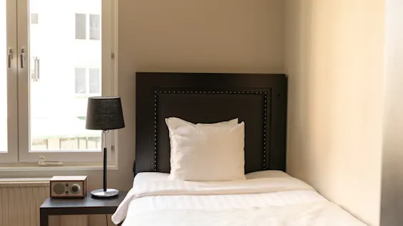 En mysig enkelsäng i ett rum på Home Hotel Tapto i Stockholm, med en mörk sänggavel, vita sängkläder och en sänglampa.