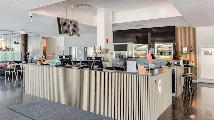 En moderne resepsjonsdisk står med datamaskiner og diverse gjenstander, omgitt av et romslig lobbyområde med sitteplasser og dekorativ belysning.