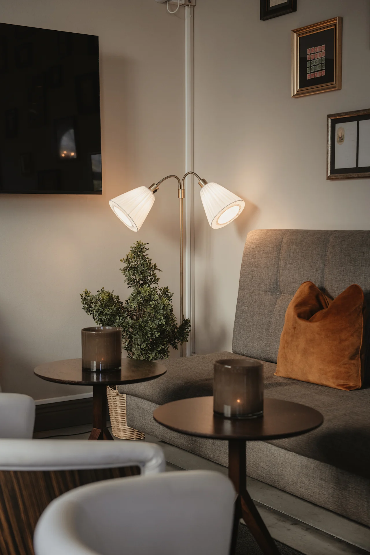 En varm och inbjudande hotellounge med en bekväm soffa, mjuk belysning från en golvlampa och dekorativa inslag.