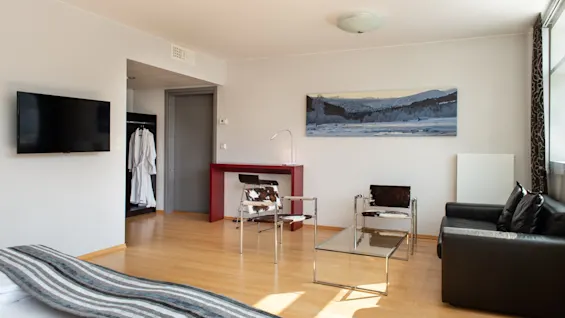 Et moderne hotelværelse med seng, tv, siddeområde med kohudsstole, en sort sofa og et naturskønt maleri.