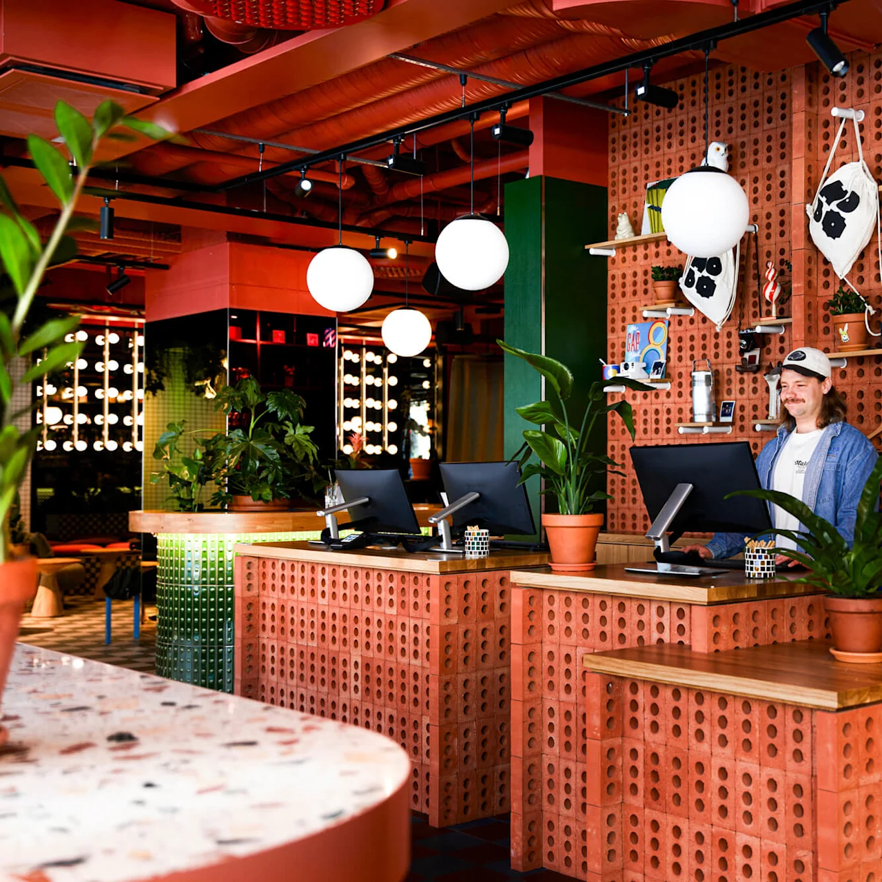 Receptionen har murstensdiske med computere og planter. En person står ved en station, omgivet af varer på hylder. Runde loftslamper oplyser det livlige rum.