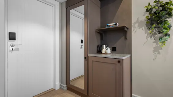 A welcoming hotel room entrance with a full-length mirror, a hospitality station, and a decorative plant.