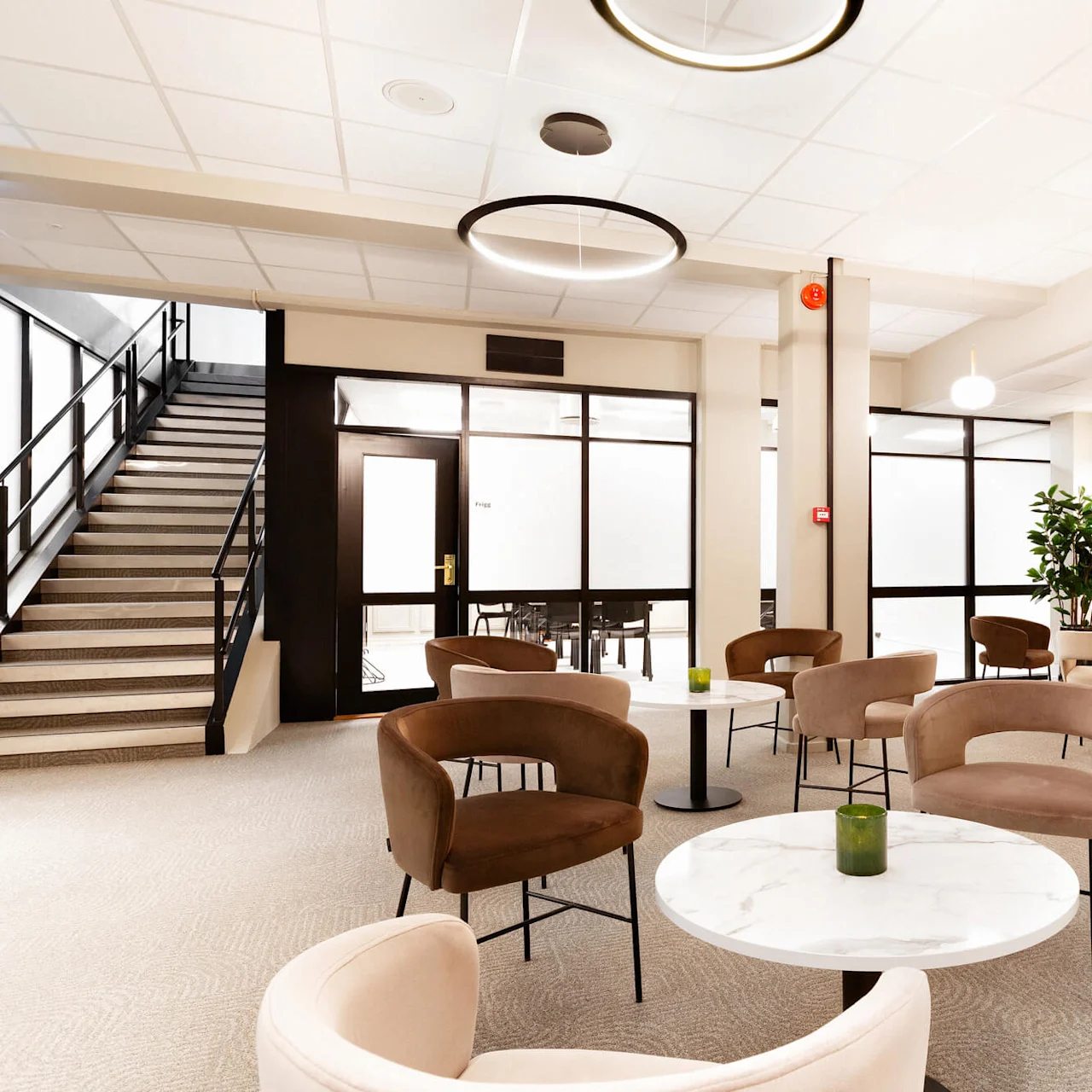 Lounge-stole omgiver marmorborde i et moderne interiør. En trappe fører opad, med planter og varme træelementer, der forbedrer rummet. Blød belysning skaber en indbydende atmosfære.