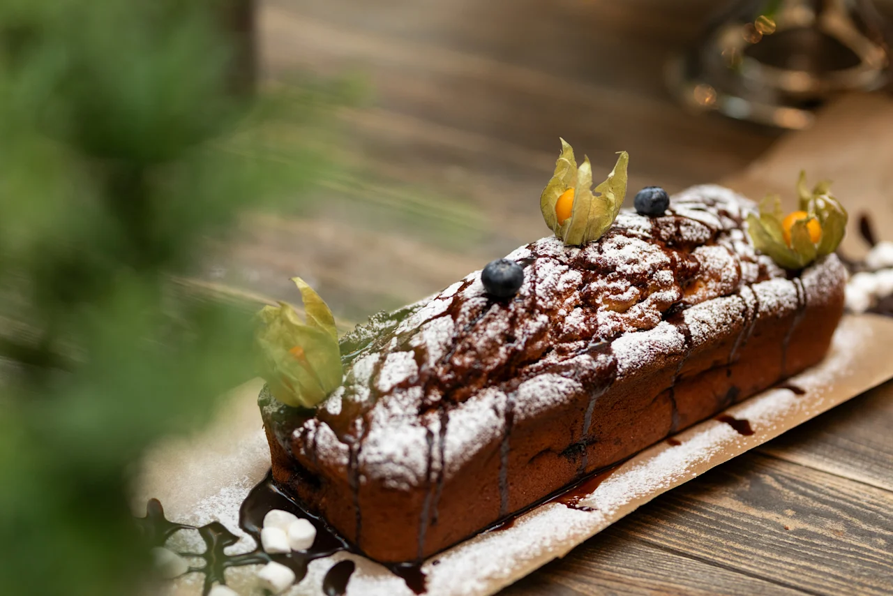 A delicious loaf cake, dusted with powdered sugar and chocolate drizzle, garnished with berries. Home Hotel Grand Bodø.