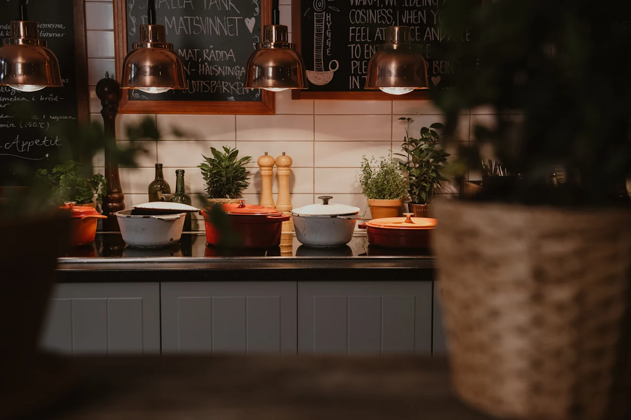 A warm kitchen counter with various cooking pots, green plants, and chalkboards displaying text like MATSVINNET and COSINESS.