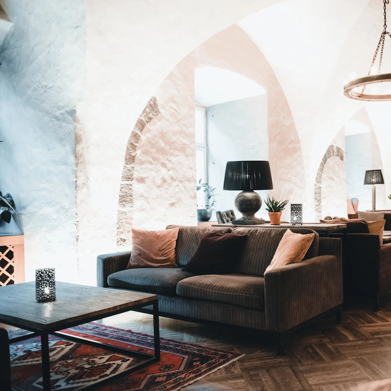 Hyggeligt siddemiljø med sofaer og puder, træborde og dekorative lamper under hvælvede lofter. Planter og et klaver forbedrer den elegante, rolige atmosfære.