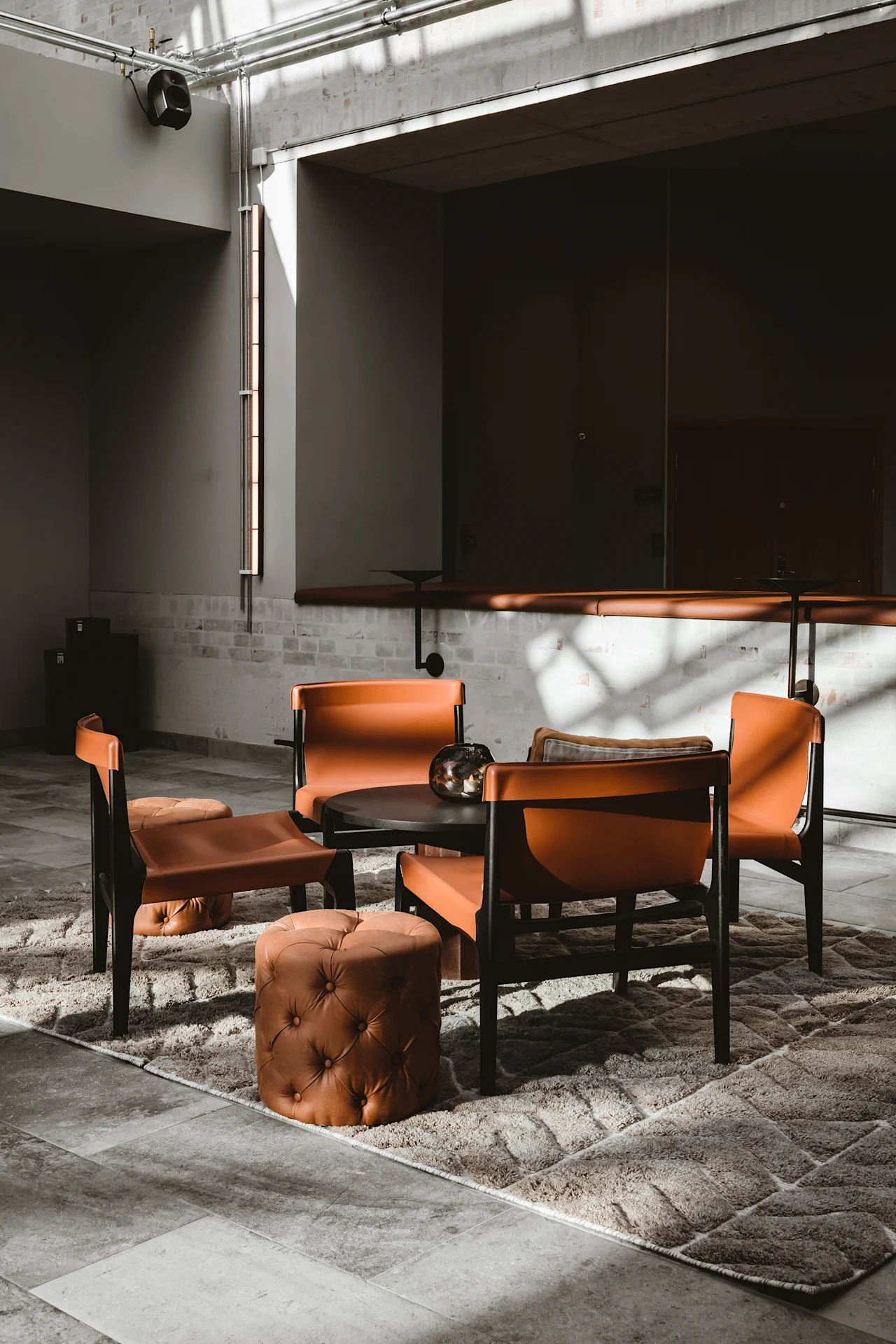 Et koselig salongområde på Quality Hotel Arlanda XPO med oransje stoler og puffer rundt et bord på et teppe, badet i sollys.