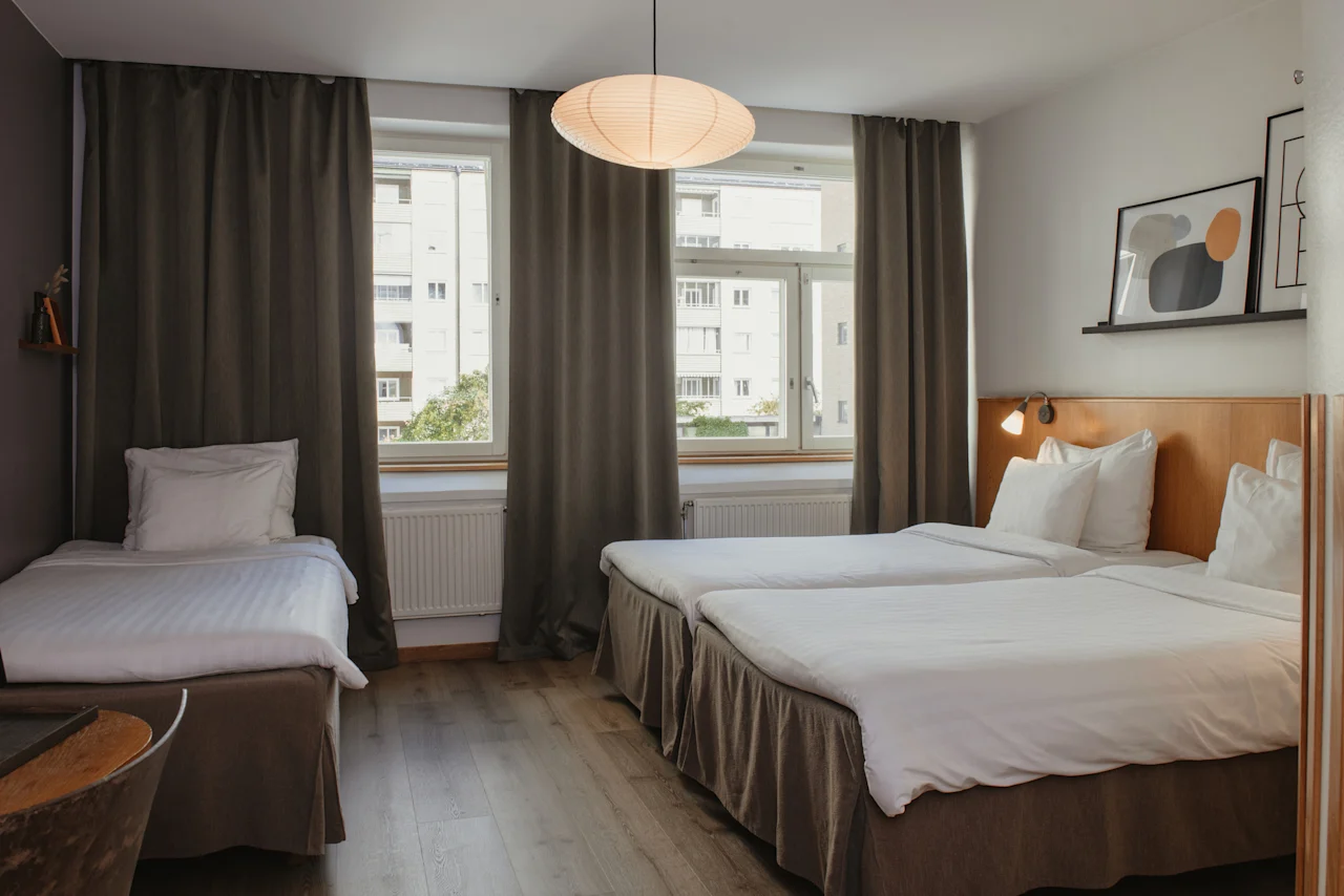 A comfortable hotel room at Home Hotel Uppsala with three beds, large windows, and contemporary wall art.