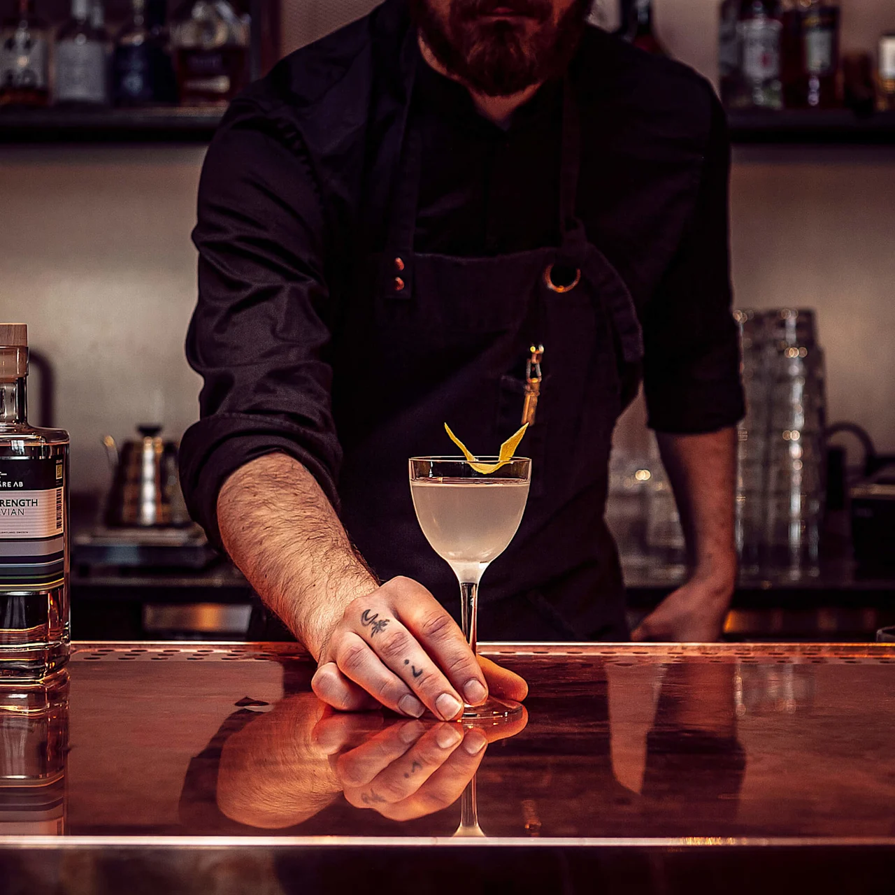 A bartender serves an artisan cocktail in a dimly-lit bar with a copper bar counter at Copperhill Mountain Lodge in Swedish ski-town Are.