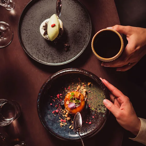 Two people enjoying beautifully plated desserts and coffee at a table, seen from above.