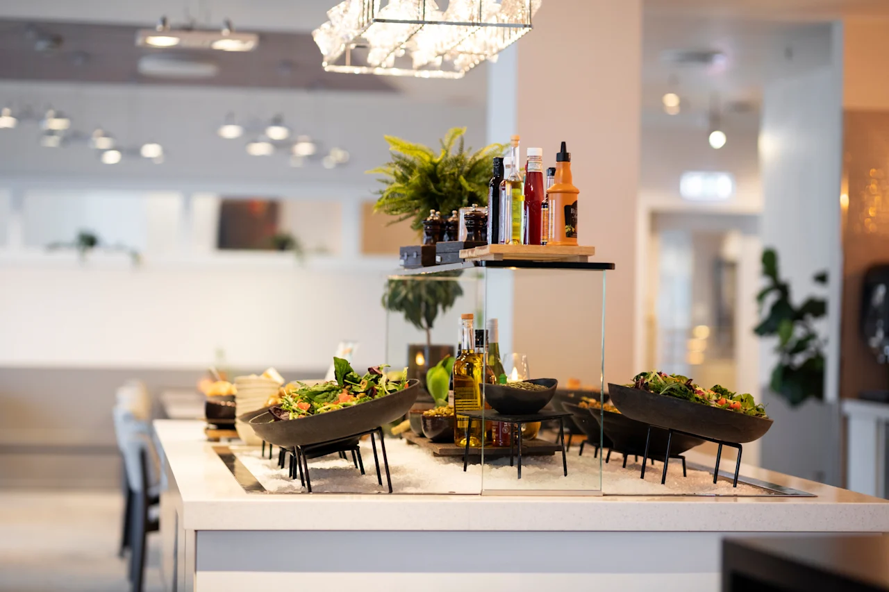 Eloisa salaattibaari tuoreilla vihanneksilla, kastikkeilla ja öljyillä, sijoitettuna moderniin ruokasaliin.