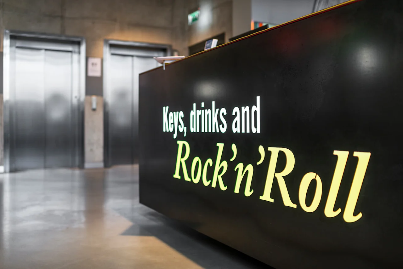 A black counter displays the text "Keys, drinks and Rock’n’Roll" in a modern lobby, with elevators in the background.