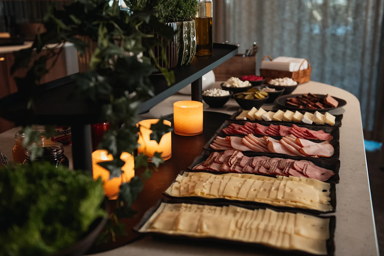 Ett vackert arrangerat buffébord med ett urval av kallskuret, ostar och tillbehör, mjukt upplyst av levande ljus.