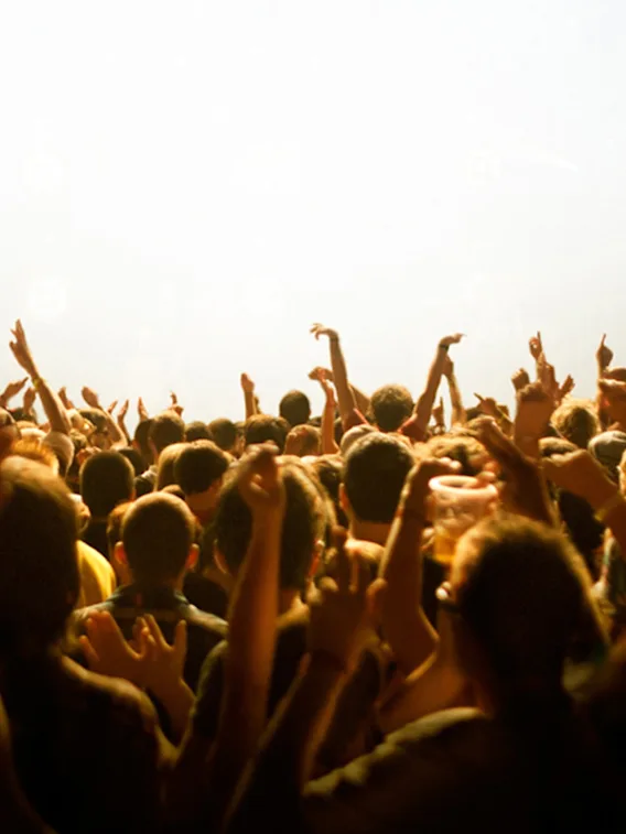 En livlig publik på en konsert eller ett evenemang, med många händer uppsträckta i spänning mot starka scenljus.