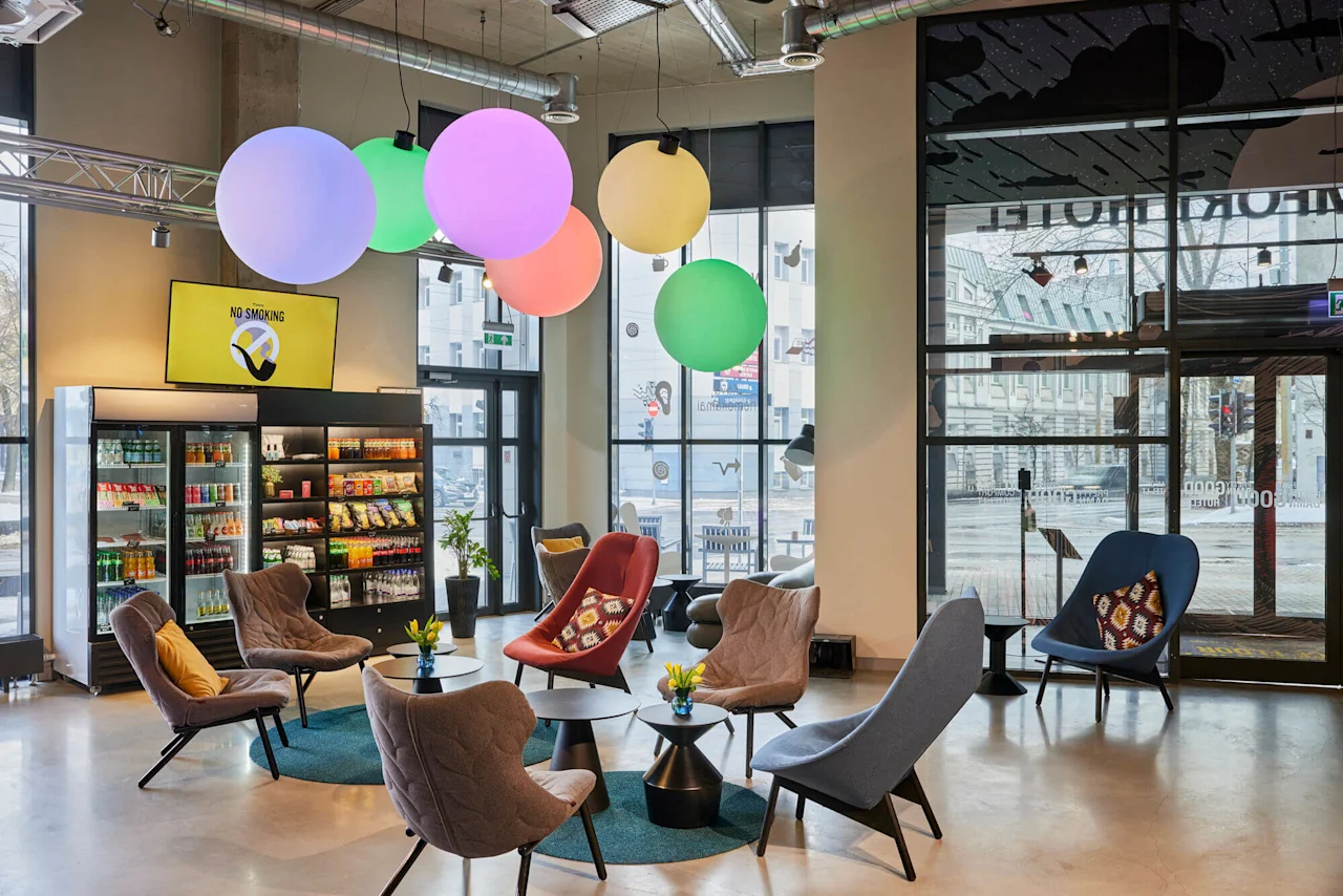 Seating area with colorful chairs encircling small tables, illuminated by large glowing spheres. A display case with snacks and drinks is in the background. "NO SMOKING" sign visible.