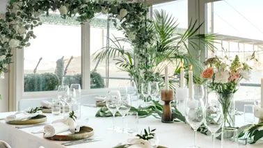 A beautifully decorated table set for a special event, featuring white flowers, lush greenery, candles, and elegant place settings.