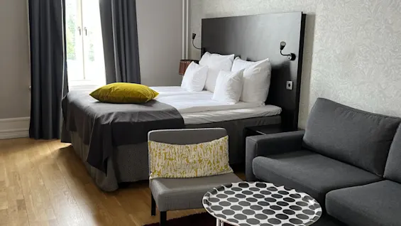 A neatly arranged hotel room with a bed, seating area, and decorative lighting.