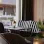 Mysig kafé sittgrupp med randig soffa och ett litet bord med lampa och vas. Stort fönster visar en parkerad bil utanför. Neutral, stilren inredning.