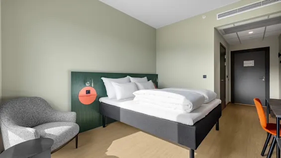 Et moderne og innbydende hotellrom med en komfortabel seng, en koselig lenestol og en funksjonell arbeidsplass.