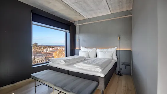 Et moderne hotellrom på Comfort Hotel Porsgrunn med en stor seng, en benk og et vindu med utsikt over byen.