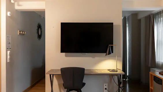 Et koselig hotellrom med et skrivebord, en lampe og en veggmontert TV, perfekt for arbeid eller avslapning.