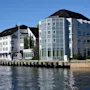 Et hotell med blå markiser og en moderne glassbygning ved vannkanten på en solrik dag. Teksten lyder Hotel.