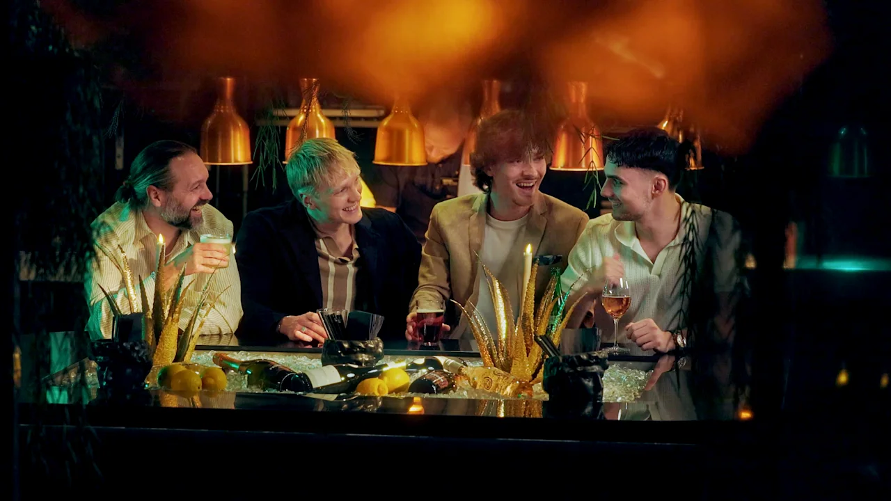 Neljä ihmistä nauraa ja seurustelee baarissa, nauttien juomia lämpimässä ja kutsuvassa ilmapiirissä.