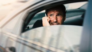 Man in a car talking on this phone looking out the window