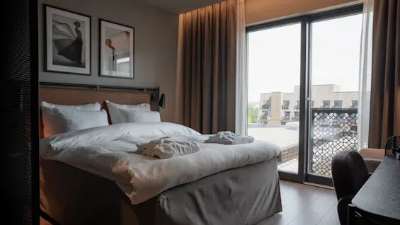 Viihtyisä hotellihuone, jossa on suuri sänky, valkoiset vuodevaatteet ja näkymä rakennuksiin. Huonetyyppi Family Connect Lily Country Clubissa.