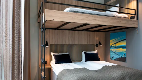 Et moderne hotellrom med en komfortabel køyeseng med en dobbeltseng nede og en enkeltseng oppe.