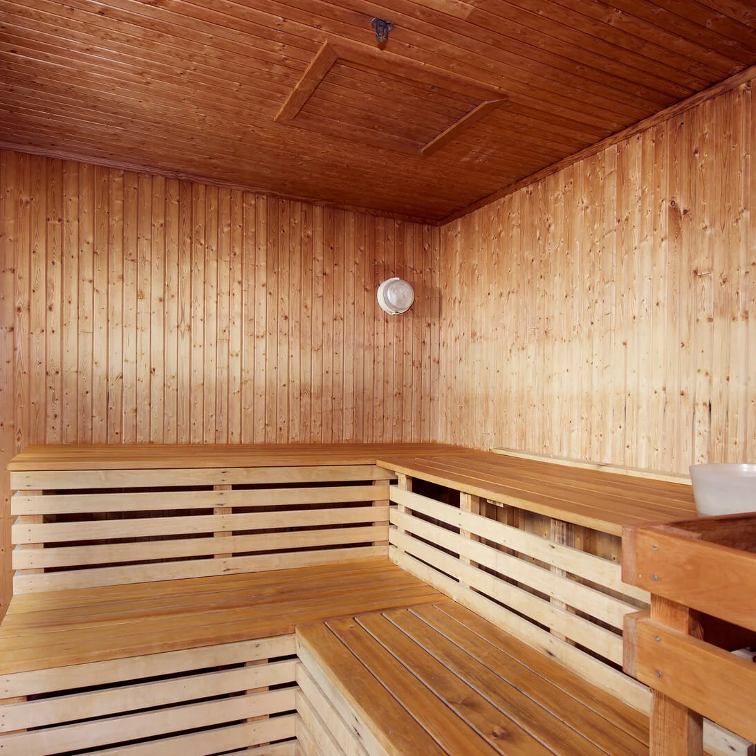 Et træbeklædt sauna-interiør med bænke og en vandspand, der formidler ro. Termometer og hygrometer viser temperatur og fugtighetskontrol.