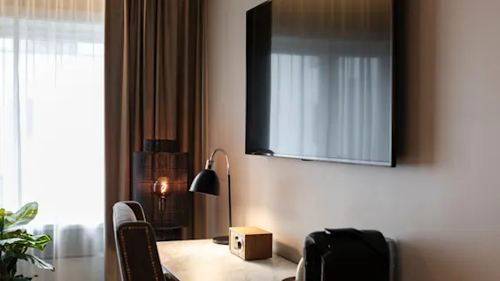 A cozy corner in a room at Home Hotel Grand Bodø, featuring a desk with a lamp and coffee machine, and a wall-mounted TV.