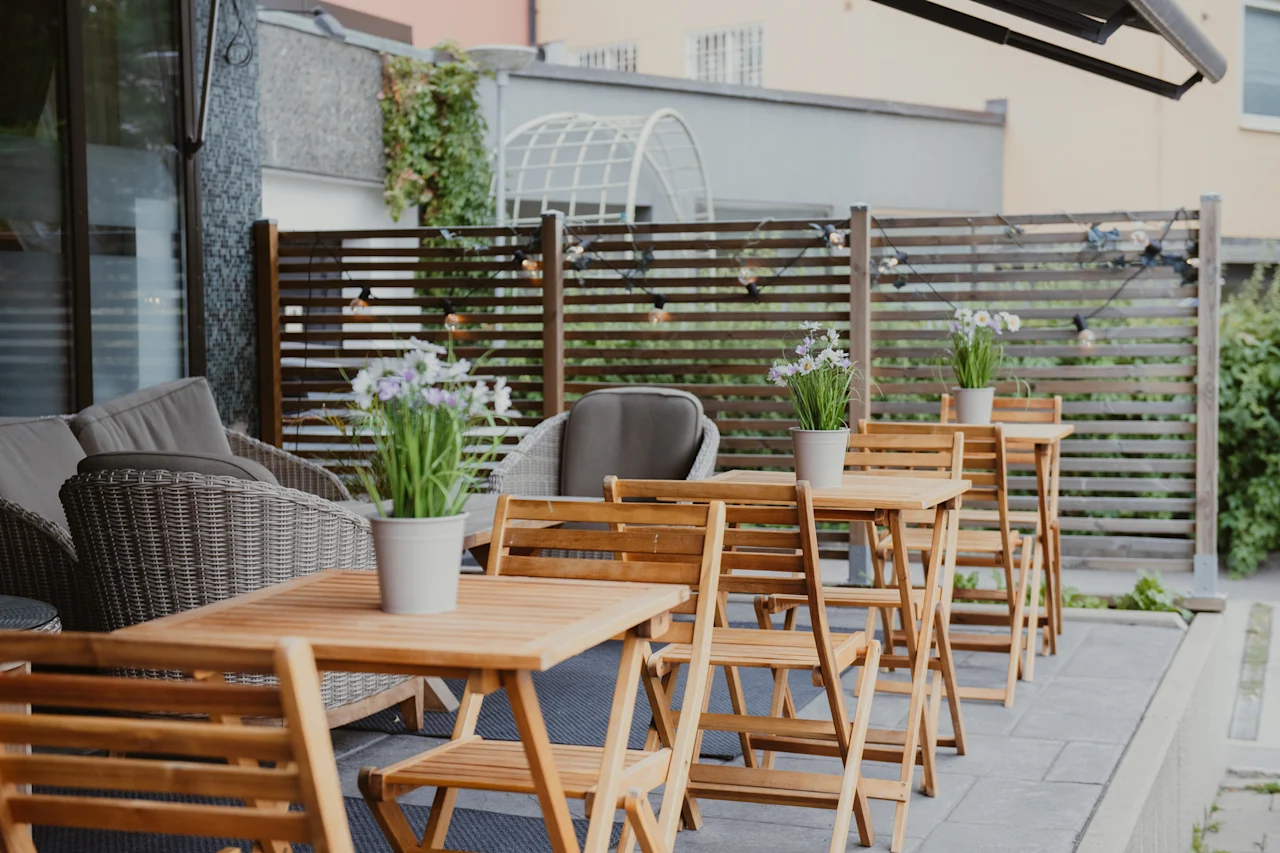 An inviting outdoor patio with wooden tables, chairs, and potted plants, perfect for a relaxing meal or gathering.