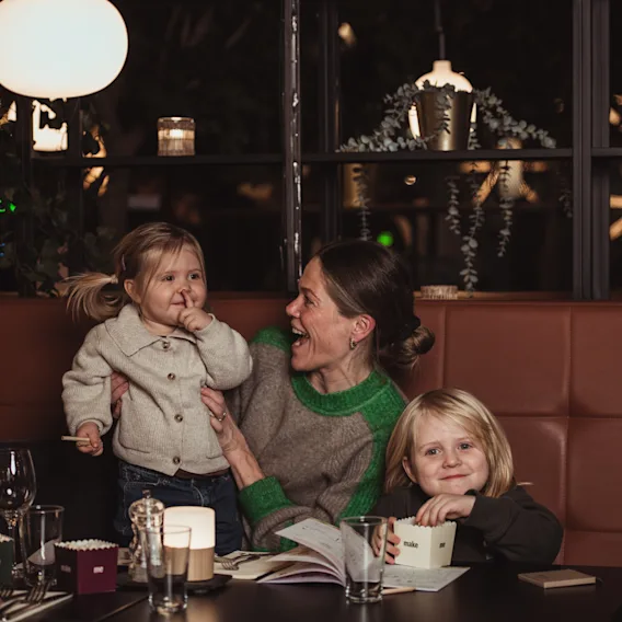 En mamma som skrattar med sina två små barn vid ett mysigt restaurangbord under middagen.