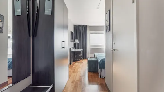 A hotel room entrance with a wardrobe displaying 'Do not disturb' and 'Please make up room' signs, leading to a bed and desk.