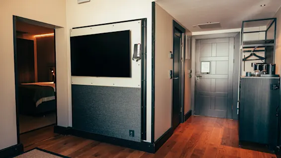 En modern hotellrumsinredning med en TV, en glimt in i sovrummet och en välkomstplats med bekvämligheter.
