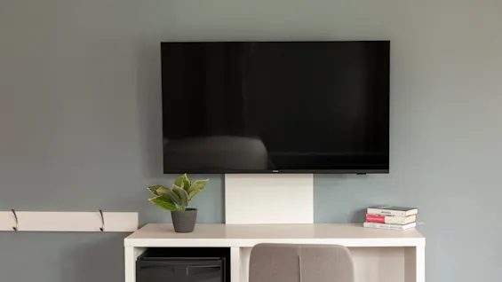 A wall-mounted television above a desk with a plant, books, and a chair, creating a functional and relaxing space.
