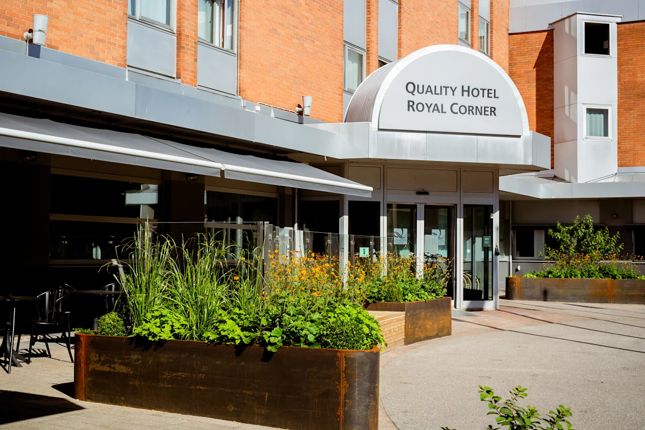 Den innbydende inngangen til Quality Hotel Royal Corner, med frodige grønne planter og et uteserveringsområde under en markise.