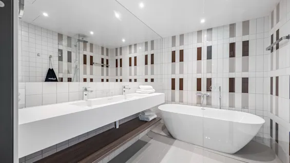 A bright, modern bathroom featuring a double vanity, a freestanding tub, and a shower, with patterned wall tiles.