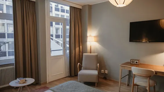 Et hyggeligt hotelværelse på Home Hotel Wellington med en seng, lænestol, skrivebord og en altandør, der fører til byudsigt.