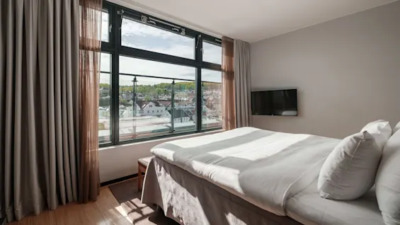 A bright hotel room at Farris bad in Larvik with a large window offering a view of the town, a comfortable bed, and a TV.