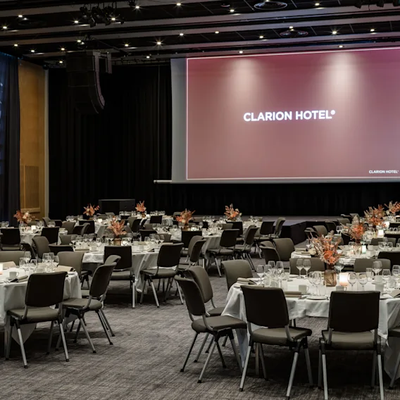 A spacious event hall with numerous round tables and chairs, elegantly set for a gathering. 
