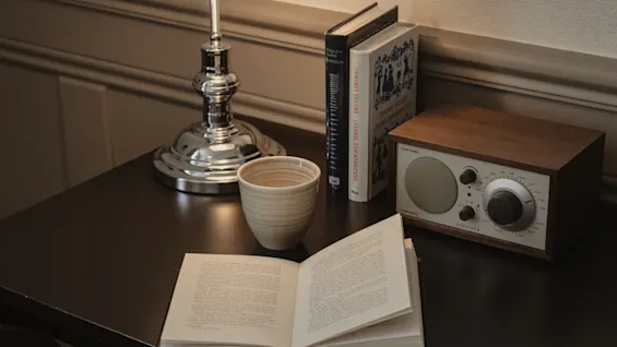 En mysig läs- eller arbetsplats med en öppen bok, en kopp och en radio på ett mörkt skrivbord, upplyst av en klassisk skrivbordslampa.