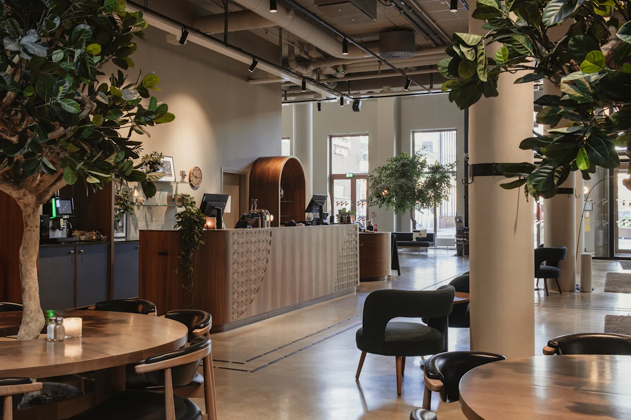 Home Hotel Tapetfabriken: A modern and inviting hotel lobby with a wooden reception desk, comfortable seating, and lush green plants.
