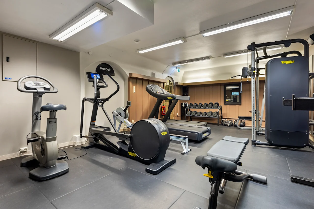 Et velutstyrt treningsstudio på Home Hotel Gabelshus med ulike treningsapparater inkludert en sykkel, ellipsemaskin, tredemølle og vekter.