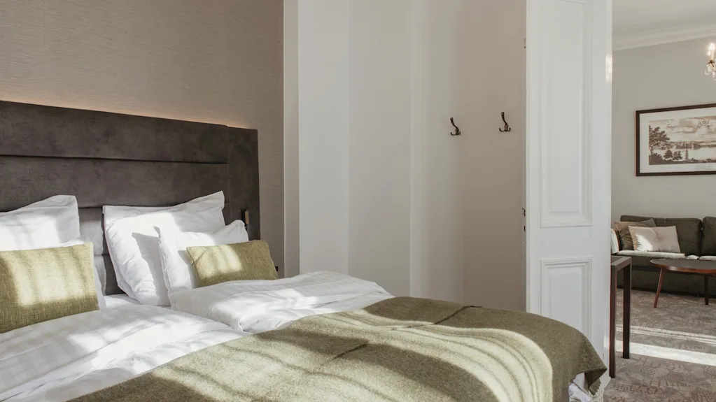 Home Hotel Victoria. Kutsuva hotellihuone, jossa kaksi pedattua sänkyä ja avoin oviaukko erilliseen oleskelutilaan.