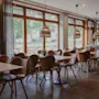 A bright and inviting restaurant dining area with many tables and chairs, large windows, and woven pendant lights.